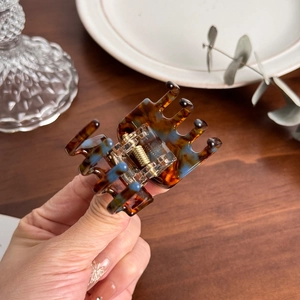 Elegant tortoiseshell acetate hair claw with blue texture and gold spring held by hand