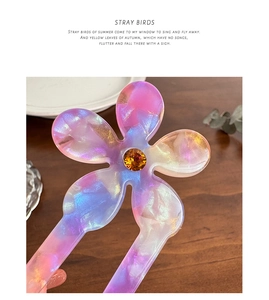 Macro detail of acetate flower hair fork with iridescent petals and orange gemstone core