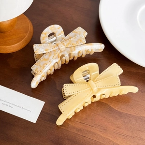 Elegant large acetate bow hair claws in yellow and marble patterns on wooden background