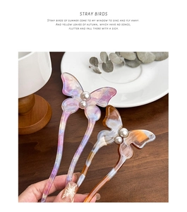 Artistic detail of acetate butterfly hair pins with white pearl accents on a wooden tray