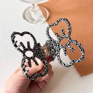 Hollow butterfly hair claw clip with black and white spotted acetate pattern held in hand