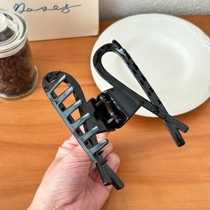 Glossy large black hair claw clip for thick hair held over a rustic wooden table