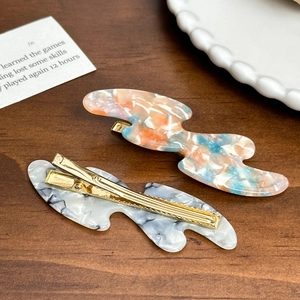 Minimalist marble acetate hair clips with gold metal duckbill grip on wood desk