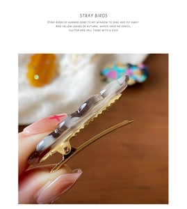 Close-up of golden metal hair clip featuring marble resin texture and spring detail