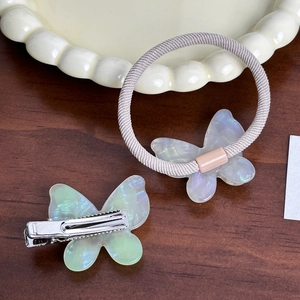 Iridescent butterfly hair clip and hair tie set on a ceramic tray for hair styling