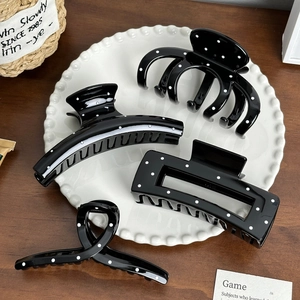 Set of four black and white polka dot hair claws in various shapes on a ceramic tray