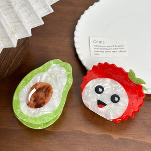 Acetate fruit-shaped hair claws featuring avocado and red litchi designs on wood