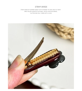 Detail view of a dark red floral hair clip showing the golden alloy sawtooth clamp and grip