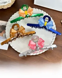 Detail view of four colorful acetate bow hair claws in an elegant white ceramic dish