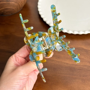 Handheld marble acetate hair claw clip with blue and yellow patterns and gold spring
