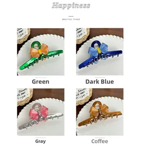 Detail of four large acetate hair claw clips with bow designs in green, blue, grey, and coffee