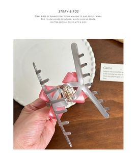 Detail showing pink bow acetate claw clip with grey translucent grip on a ceramic plate