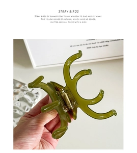Dettaglio di un fermaglio per capelli in acetato verde oliva con robusta molla d'oro