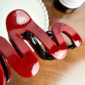Glossy red S-shaped hair claw clip for elegant bun hairstyles on a textured background