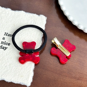 Set aus roter Acryl-Bärenhaarklammer und Haargummi auf minimalistischem Holzuntergrund