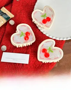 Detail view of heart-shaped acetate hair claw with red cherry prints on red knit sweater