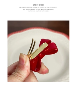Detail view of red acetate bow hair clip with gold metal clip and logo embossing