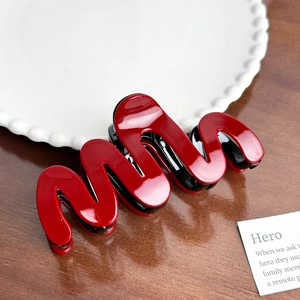Glossy red wave-shaped large hair claw clip with black teeth on wooden background