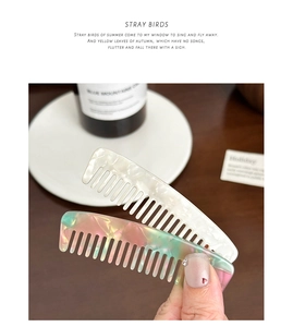 Detail view of two mini acetate hair combs with pearlescent finish on wooden desk