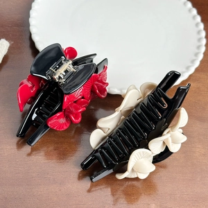 Elegant black hair claw clips with red and white floral accents on a ceramic plate