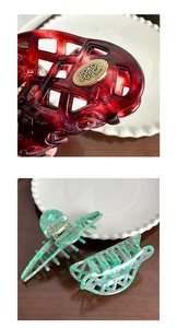Detail of hollow marble acetate hair claw clips with gold metal logo in red and mint colors