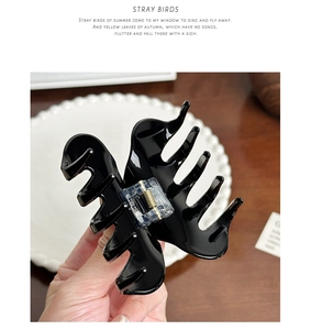 Detail of glossy black large claw clip with metal spring mechanism held by hand