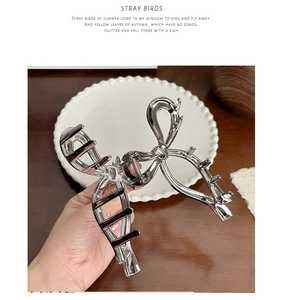 Detail view of large silver metal ribbon hair claw clip held by hand against a pearl tray