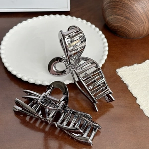 Set of two silver hollow metal hair claw clips with mirror finish on dark wood background