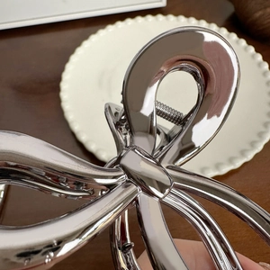 Silver metallic bow hair claw clip with mirror finish on white decorative plate