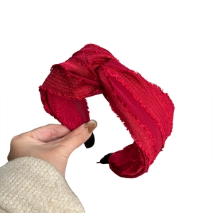 Vintage red pleated fabric headband with knot design and frayed edges on white background