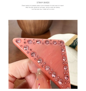 Détail macro d'une pince à cheveux triangle rose en acétate avec strass et texture marbrée