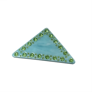 Barrette triangle en acétate bleu avec strass verts scintillants sur fond blanc