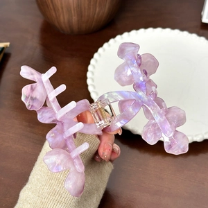 Iridescent purple flower hair claw clip in acetate resin held by hand for elegant hair styling