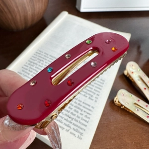 Fermaglio ovale bordeaux con strass colorati su base in metallo dorato ondulato