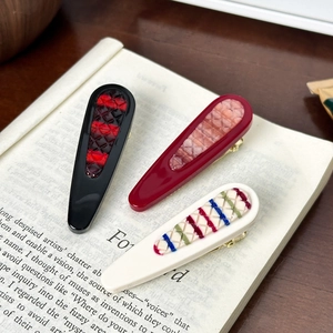 Three vintage plaid pattern resin hair clips on a book page with a retro academy style