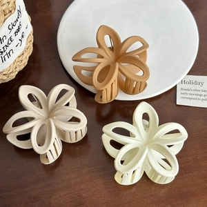 Elegant hollow plumeria hair claws in matte colors displayed on a rustic wooden table
