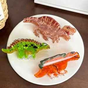 Drei bunte Haarklammern aus Acryl in Dinosaurierform auf einem weißen Teller serviert