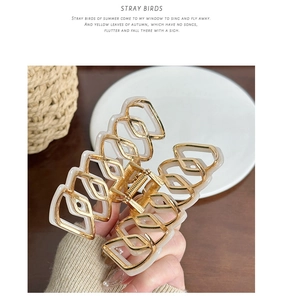 Detail view of a hollow geometric hair claw clip with gold metal and beige resin inlay