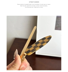 Détail de la pince à cheveux en acétate à damier avec base en métal doré tenue en main