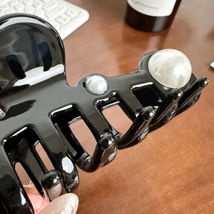 Oversized black glossy acetate shark clip with pearl accents on a wooden desk