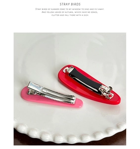 Détail de barrettes à cheveux en acétate rouge et rose sur une assiette en céramique