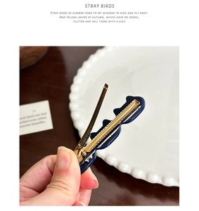 Detailed close-up of dark blue acetate hair clip with golden metal duckbill structure