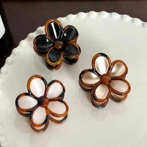 Three elegant flower hair clips in black, cream, and champagne gold on a ceramic plate