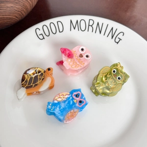 Mini owl and turtle acetate hair clips in a white ceramic dish on a wooden table