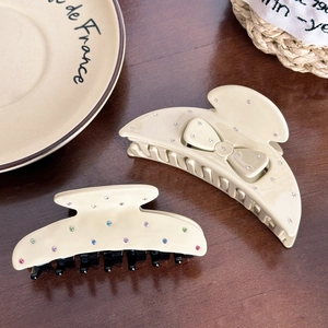 Beige acetate hair claws with rhinestones and bow design on rustic wooden background