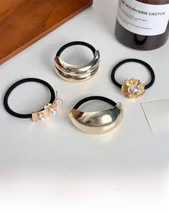 Detail of four high-elasticity hair ties with gold accents and pearls on a wooden tray