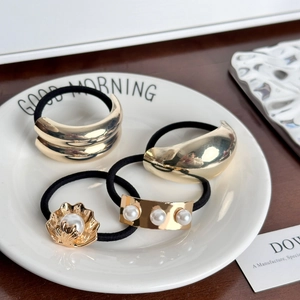 Set of 4 vintage golden metal hair ties with pearls on an elegant white ceramic plate