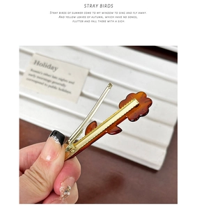 Detail view of floral acetate hair clip with amber texture and gold metal duckbill grip