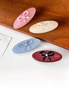 Close-up of four elegant acetate oval hair clips with sparkling bow accents on wood stand