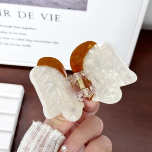 Cute butterfly acetate claw clip with cream marble and amber patterns on a wooden table